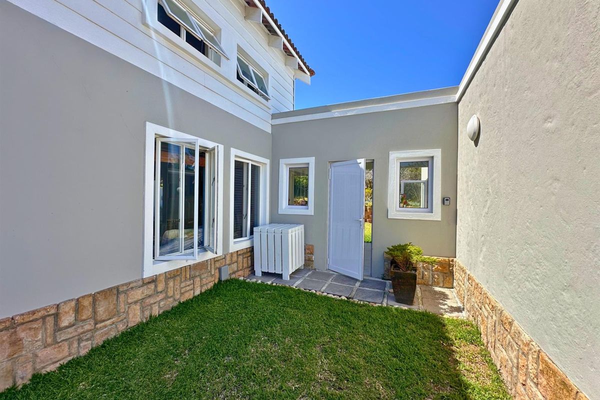 A well-maintained rear courtyard featuring stone cladding, a small lawn, and paved access to the building entrance.