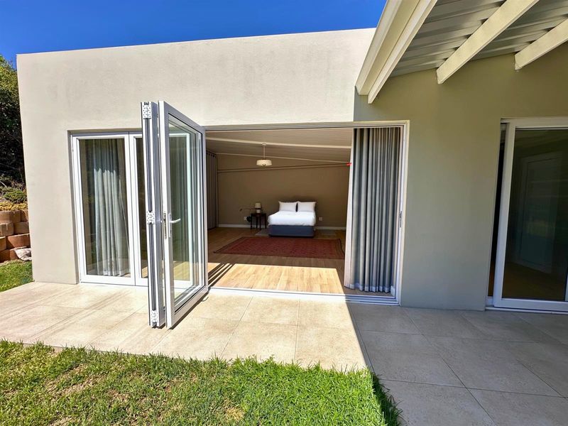 A view of a modern bedroom interior from a tiled rear patio, featuring large bi-fold doors that provide seamless indoor-outdoor flow.