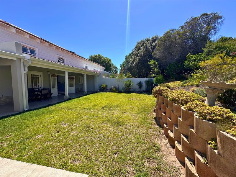 A spacious rear garden featuring a covered patio, a well-maintained lawn, and a tiered retaining wall with established landscaping.