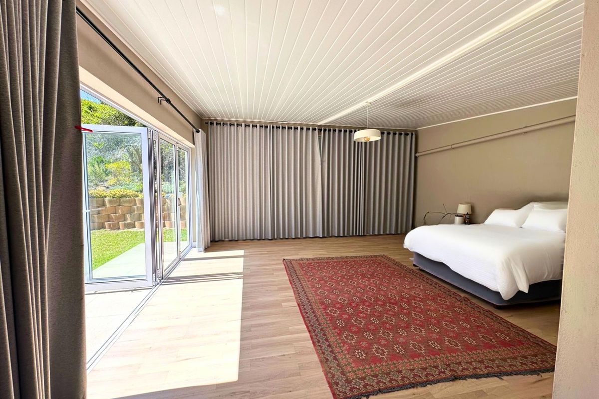 Spacious bedroom featuring light timber-look flooring, a tongue and groove ceiling, and large bi-fold glass doors providing direct access to the garden.