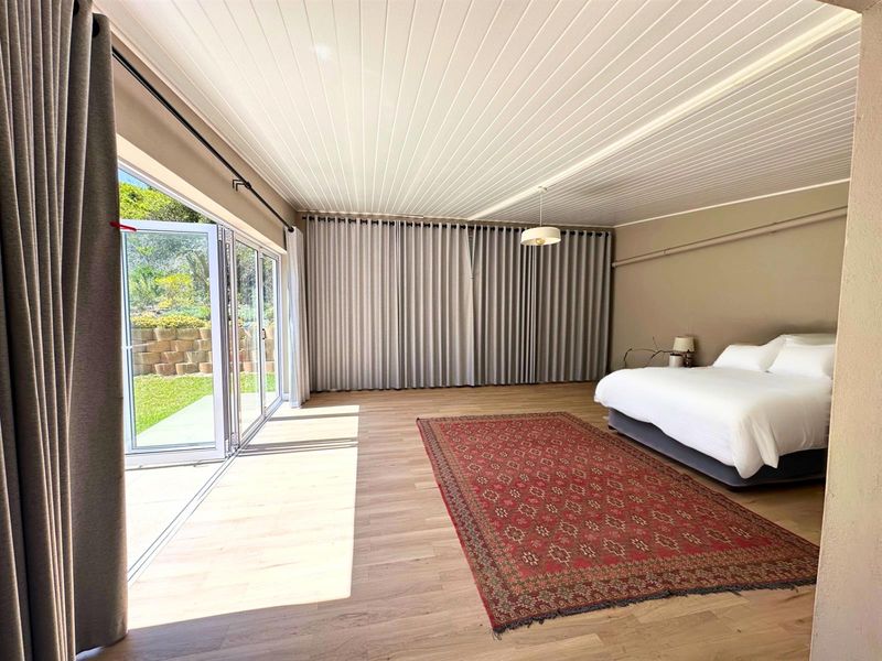 Spacious bedroom featuring light timber-look flooring, a tongue and groove ceiling, and large bi-fold glass doors providing direct access to the garden.