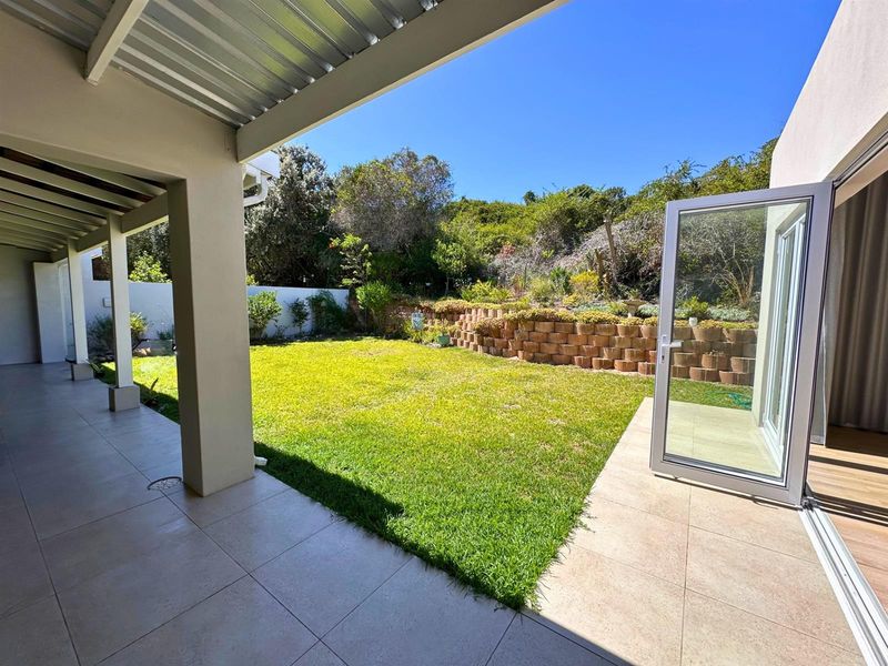 A spacious covered patio featuring tiled flooring, leading out to a well-maintained garden with a tiered retaining wall and lush greenery.