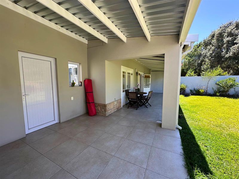 A spacious covered patio featuring tiled flooring, stone cladding accents, and direct access to the garden through sliding doors.