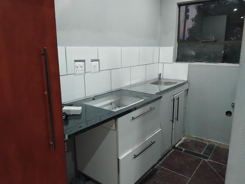 A compact kitchen area featuring white cabinetry, granite countertops, and a stainless steel sink, currently requiring finishing touches and appliance installation.