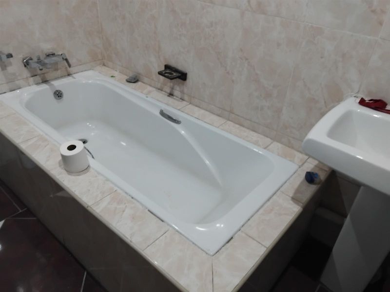 A functional bathroom featuring a built-in bathtub with wall-mounted mixer taps and a pedestal basin, finished with neutral wall tiling.