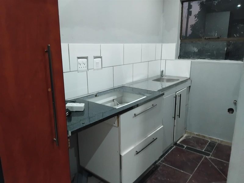 A compact kitchen area featuring granite countertops, a stainless steel sink, and white cabinetry, currently requiring completion of wall finishes and appliance installation.