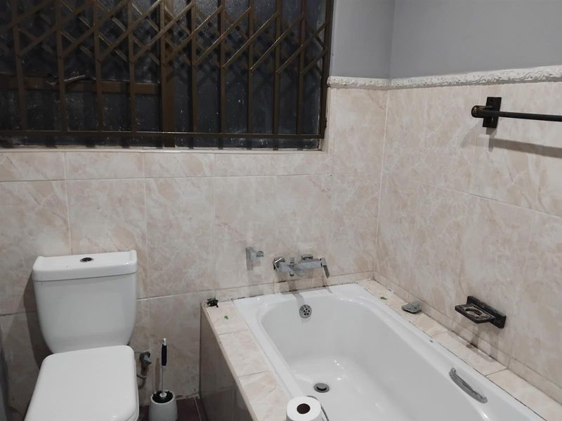 A functional bathroom featuring a built-in bathtub, toilet, and tiled walls, equipped with a security gate over the window.