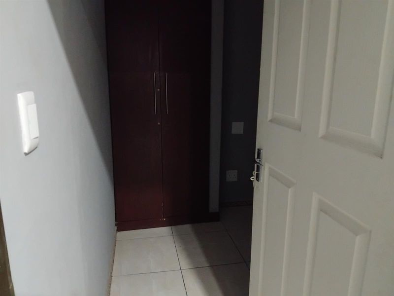 A simple bedroom interior featuring tiled flooring and a built-in dark wood cupboard, presented in a clean, vacant state.