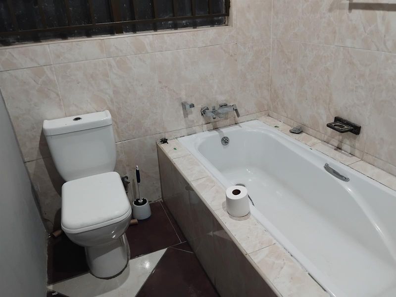 A functional bathroom featuring a built-in bathtub, toilet, and tiled finishes. The space would benefit from cosmetic updates to improve its overall condition.