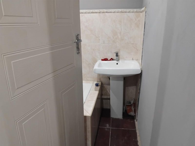 A compact bathroom featuring a pedestal basin and built-in bathtub, currently requiring finishing touches to the wall tiling and surrounding surfaces.