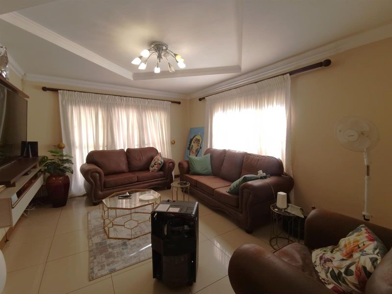 A comfortable living room featuring tiled flooring, recessed ceiling detailing, and large windows with curtain rods, providing a bright and functional living space.