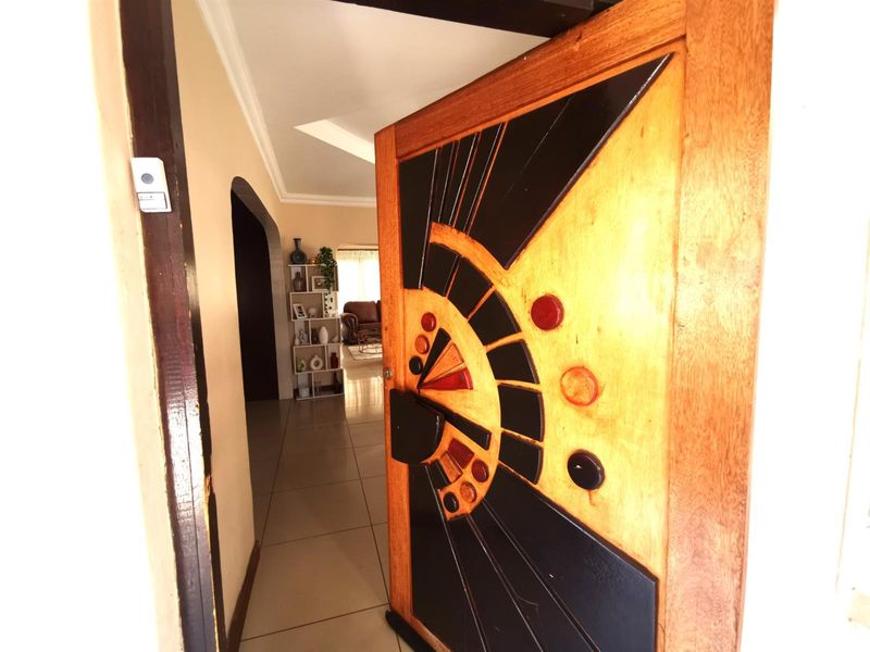 A view through a decorative wooden front door into the interior hallway with tiled flooring and an arched entryway leading to the living area.
