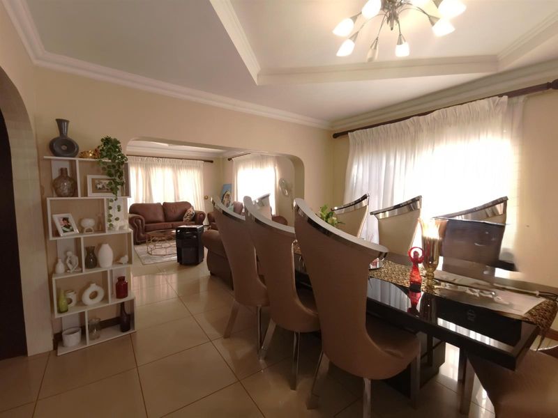 An open-plan living and dining area featuring tiled flooring, recessed ceiling detailing, and large windows with sheer curtains, creating a bright and connected space.
