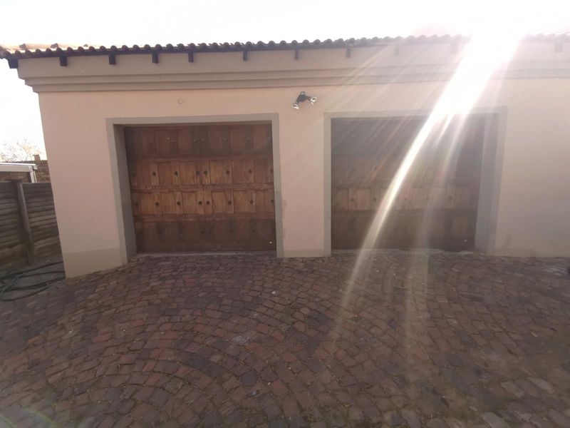 A double garage featuring traditional wooden doors and a paved driveway, set against a neutral exterior facade.