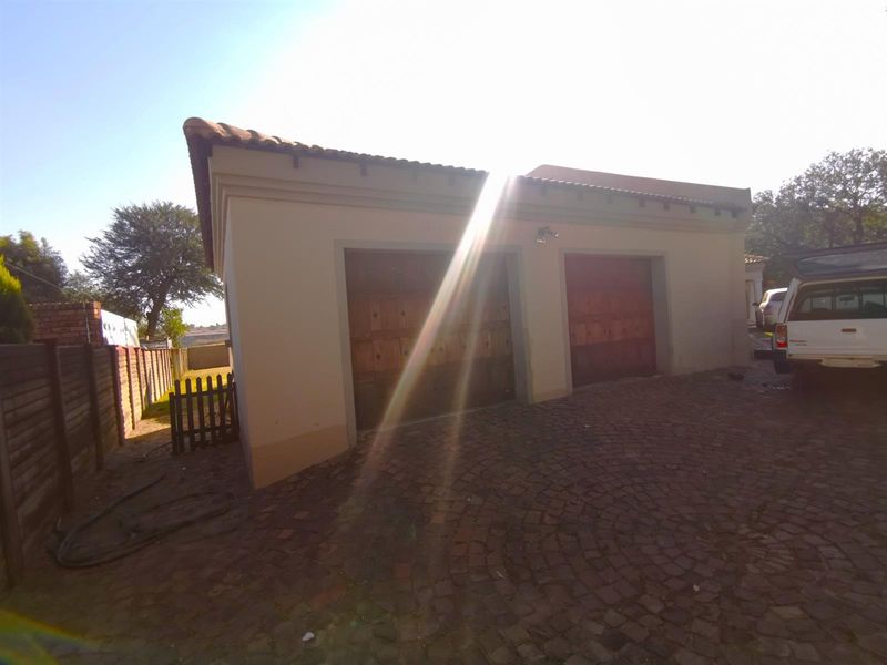 A double garage with wooden doors and a paved driveway, featuring a tiled roof and exterior lighting.