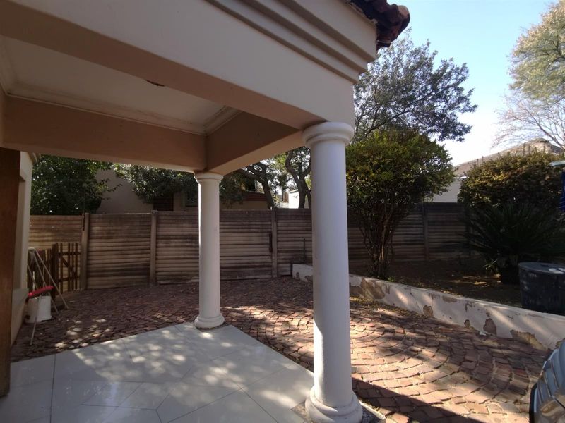 A covered patio area featuring classic columns, tiled flooring, and a paved outdoor space overlooking the garden.