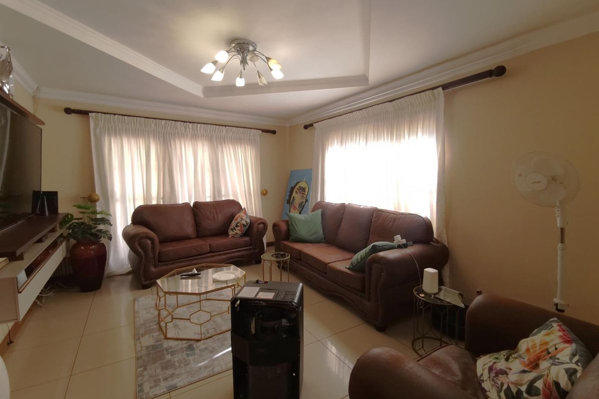 A comfortable living room featuring tiled flooring, recessed ceiling detailing, and large windows with curtain rods, providing a bright and functional living space.