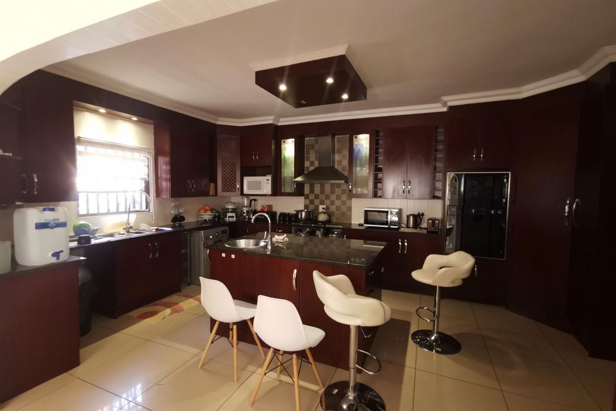 Spacious kitchen featuring dark wood cabinetry, granite countertops, a central island with a sink, and integrated stainless steel appliances.