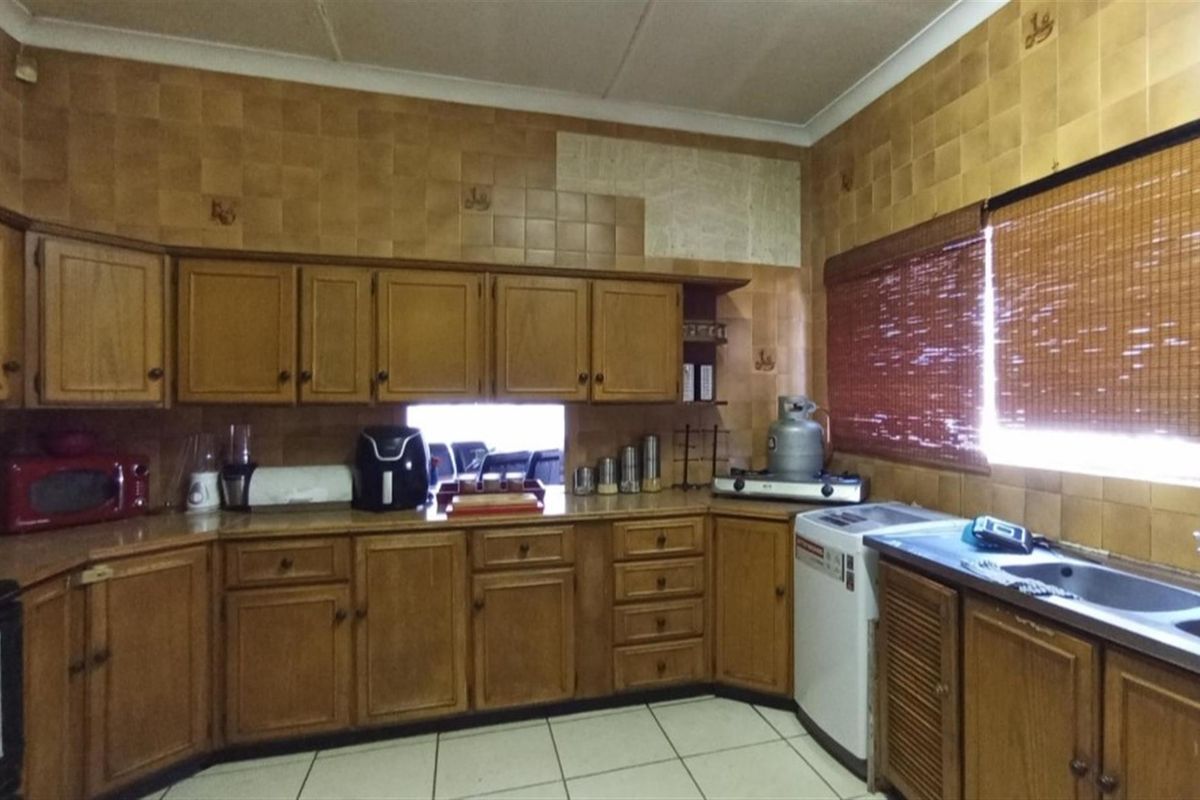 A dated kitchen featuring wooden cabinetry, tiled walls with some missing sections, and a stainless steel sink.