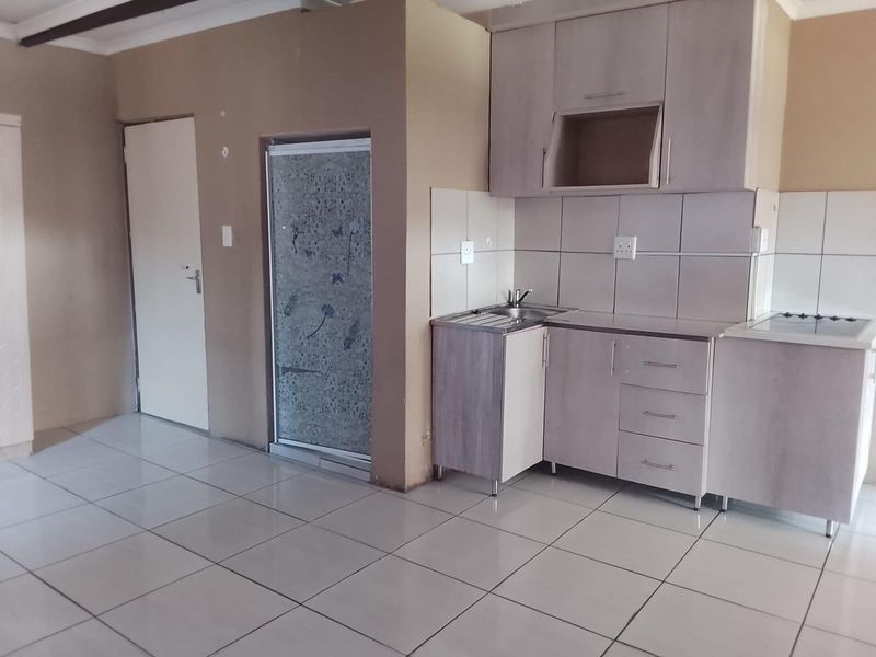 Compact kitchen area featuring tiled flooring, built-in cabinetry with a stainless steel sink, and an integrated electric hob.