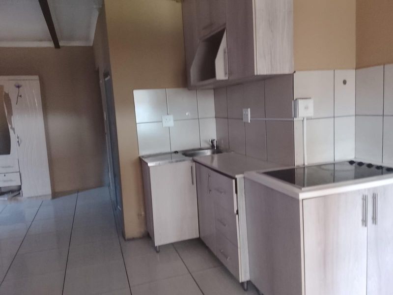 A compact kitchen area featuring built-in cabinetry, a tiled backsplash, and a ceramic hob, with tiled flooring throughout.