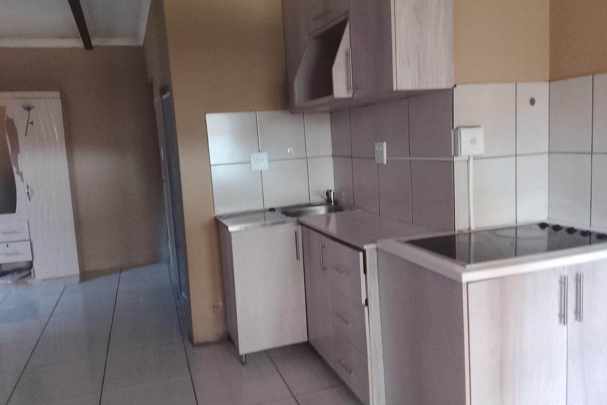 A compact kitchen area featuring built-in cabinetry, a tiled backsplash, and a ceramic hob, with tiled flooring throughout.