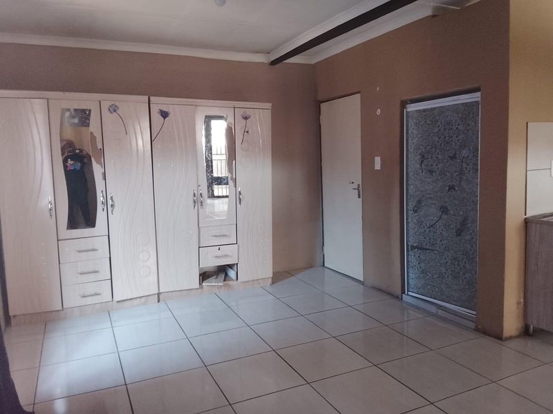 A bedroom featuring tiled flooring, built-in cupboards with some damage, and an integrated shower enclosure.