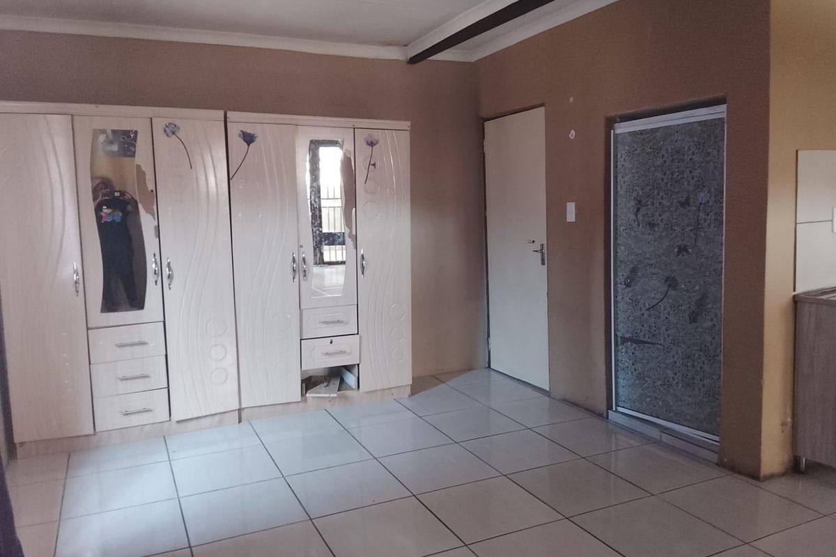 A bedroom featuring tiled flooring, built-in cupboards with some damage, and an integrated shower enclosure.