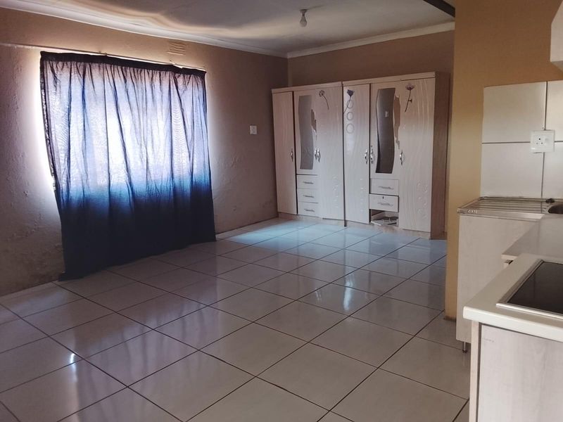 Open plan living area featuring tiled flooring, built-in cupboards, and a compact kitchen workspace with a hob and sink.