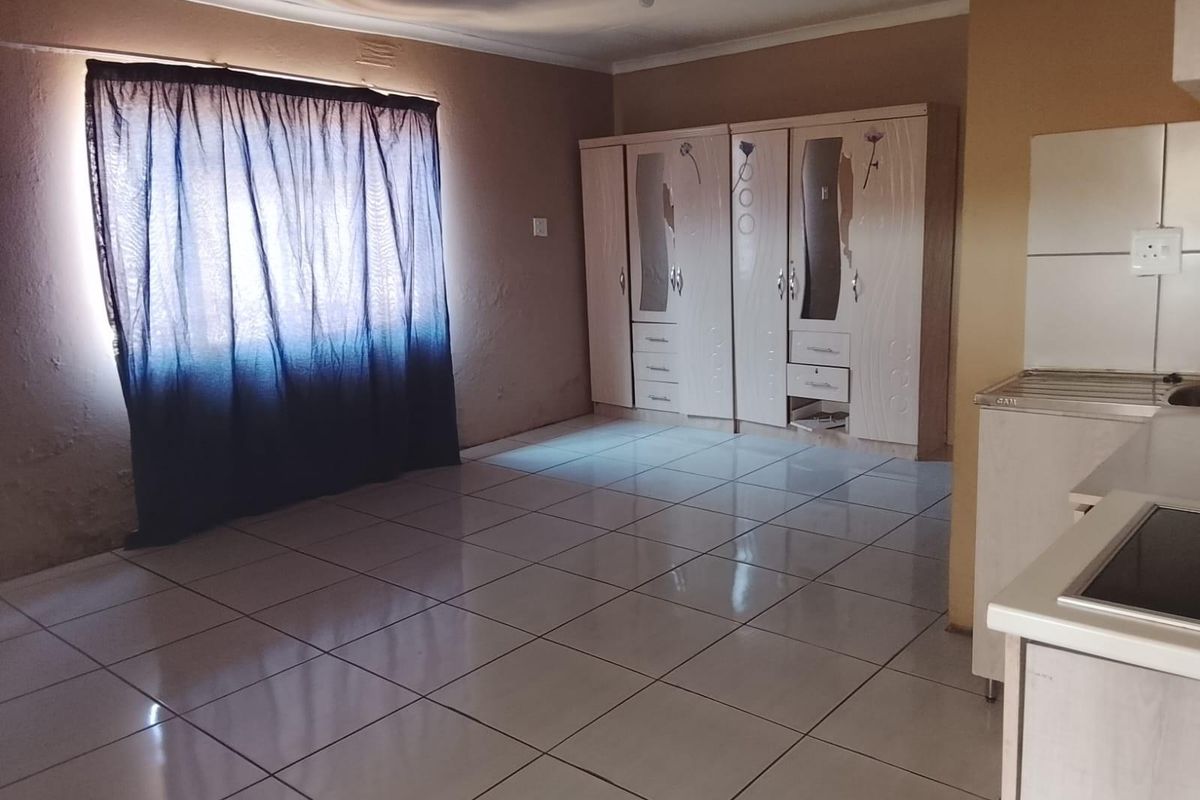 Open plan living area featuring tiled flooring, built-in cupboards, and a compact kitchen workspace with a hob and sink.