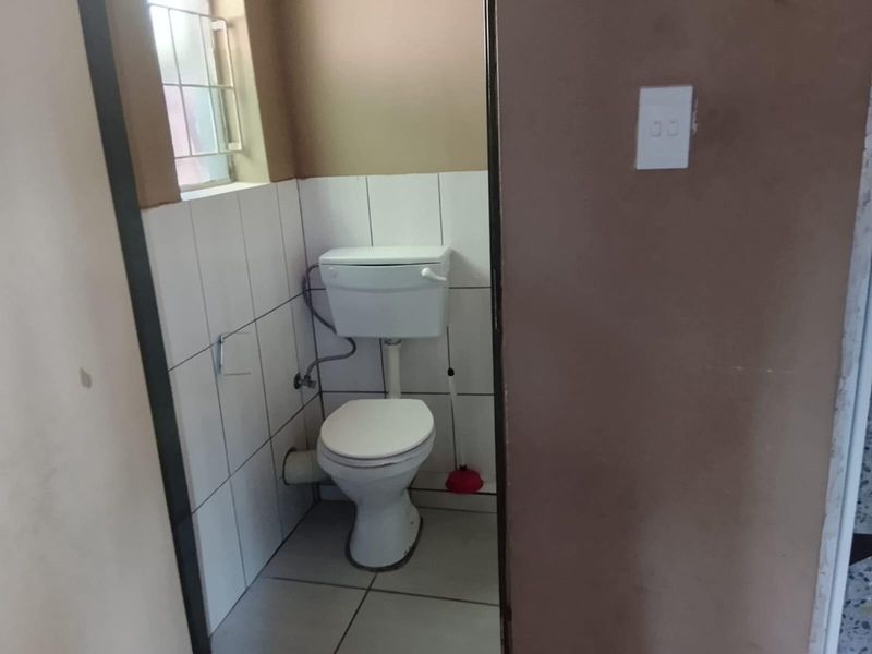A compact bathroom featuring a standard toilet, tiled walls, and tiled flooring, requiring minor cosmetic updates to improve its overall condition.