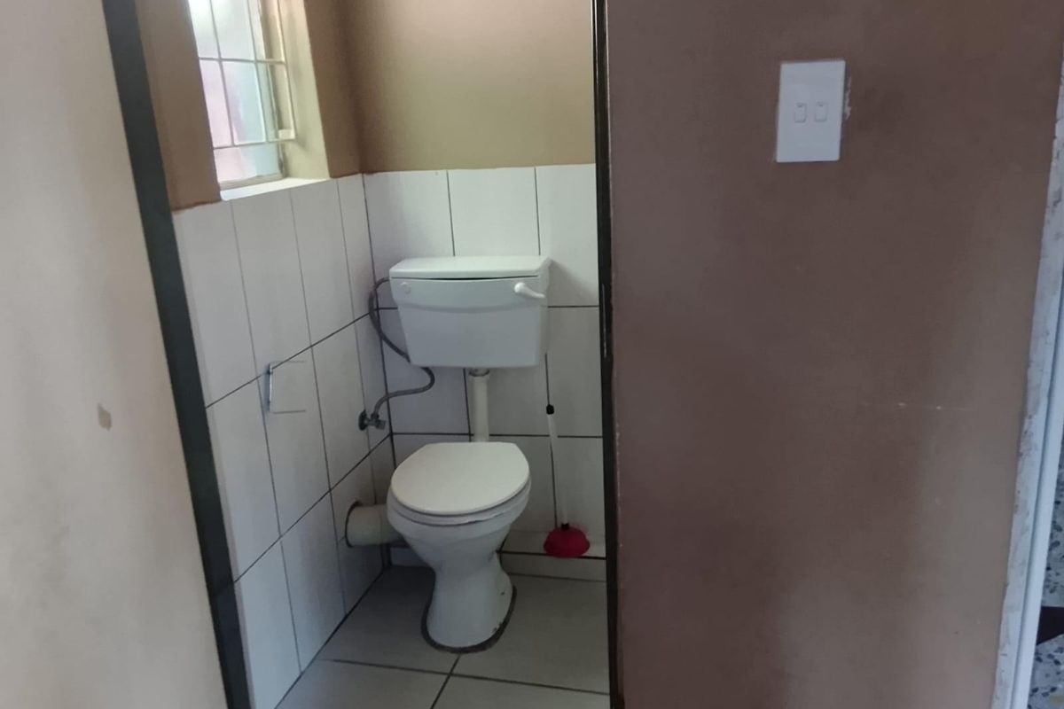 A compact bathroom featuring a standard toilet, tiled walls, and tiled flooring, requiring minor cosmetic updates to improve its overall condition.