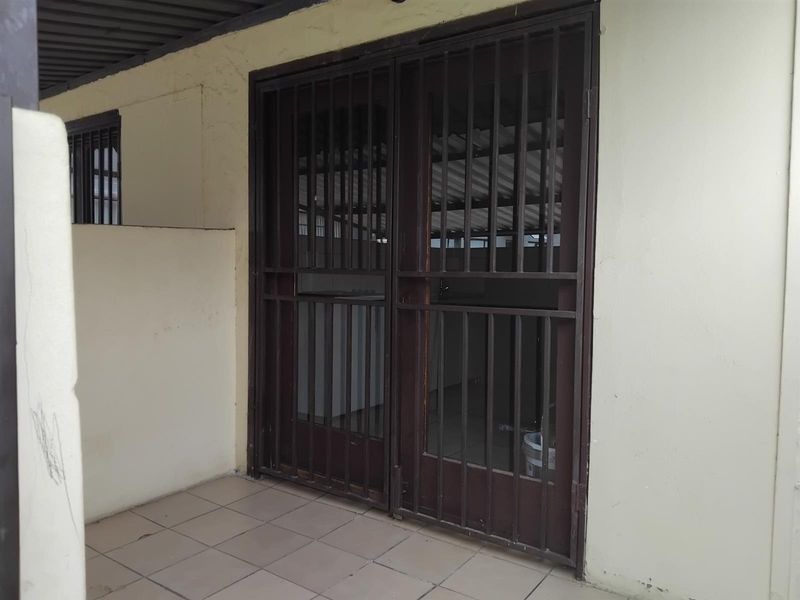 A covered patio area featuring tiled flooring and a secure metal gate entrance, showing signs of wear on the exterior walls.