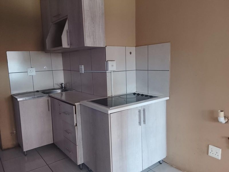 Compact kitchen area featuring light wood-tone cabinetry, a built-in electric hob, stainless steel sink, and tiled splashback finishes.