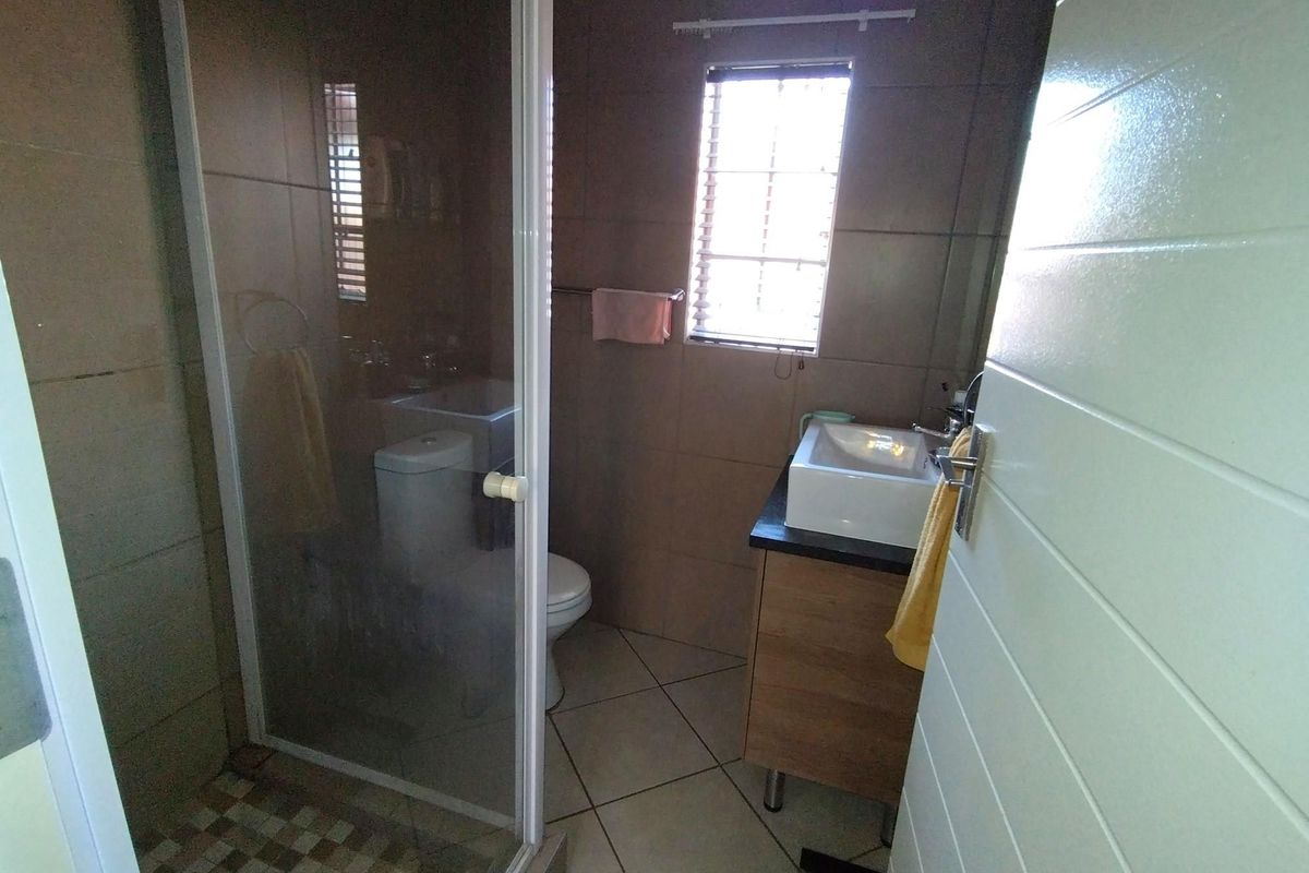 A functional bathroom featuring a shower enclosure, a modern vessel sink with a vanity cabinet, and tiled finishes throughout.