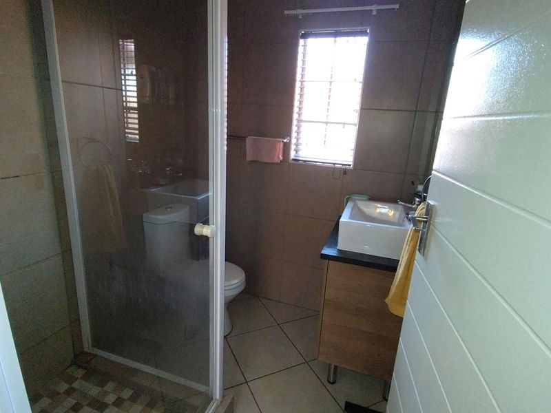 A functional bathroom featuring a shower enclosure, a modern vessel sink with a vanity cabinet, and tiled finishes throughout.
