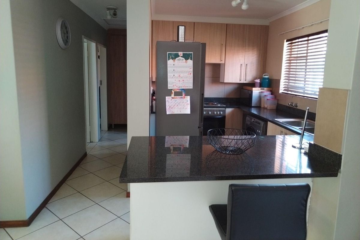 Functional kitchen featuring granite countertops, built-in cabinetry, and integrated appliances, with a breakfast bar overlooking the adjacent hallway area.