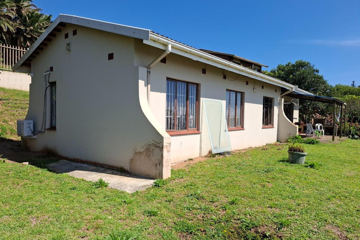 Rear exterior view of the house featuring a simple facade, metal window frames, and a small attached patio area set within a grassed garden.