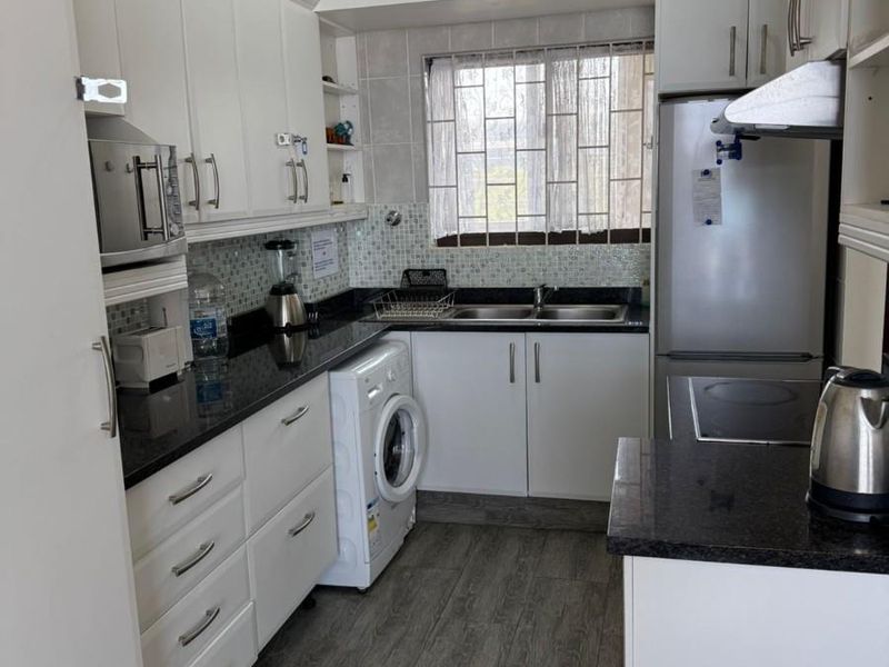 A functional kitchen featuring white cabinetry, granite countertops, a double basin sink, and integrated laundry plumbing with a tiled backsplash.