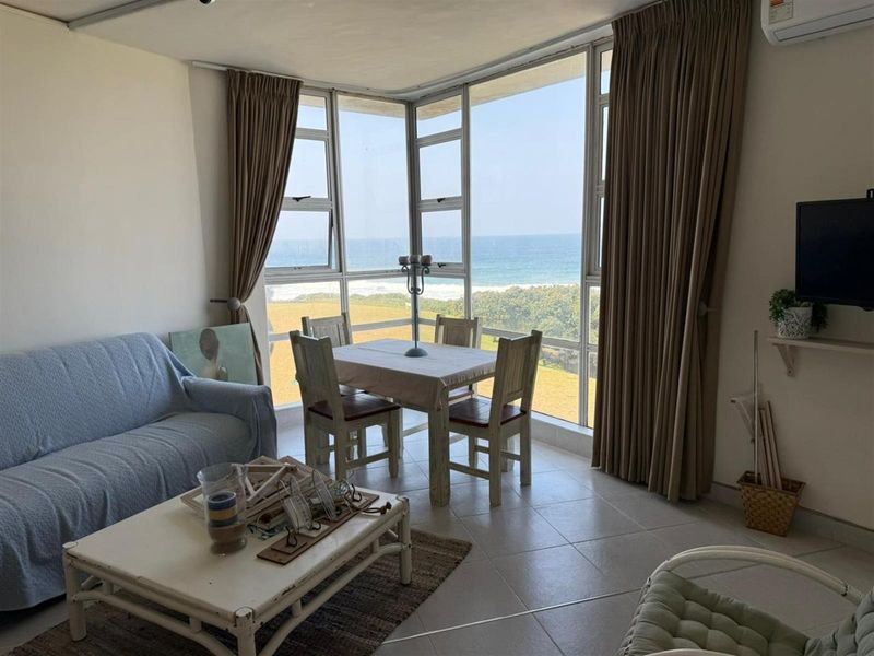 A bright living area featuring large windows with panoramic ocean views, tiled flooring, and a wall-mounted air conditioning unit.