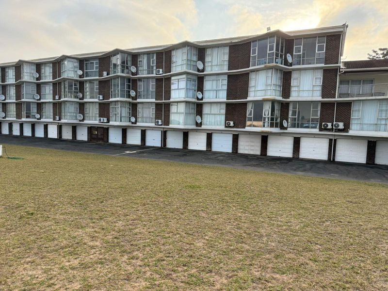 Rear view of a multi-story apartment complex featuring a row of ground-level garages, enclosed balconies, and brick facade construction.