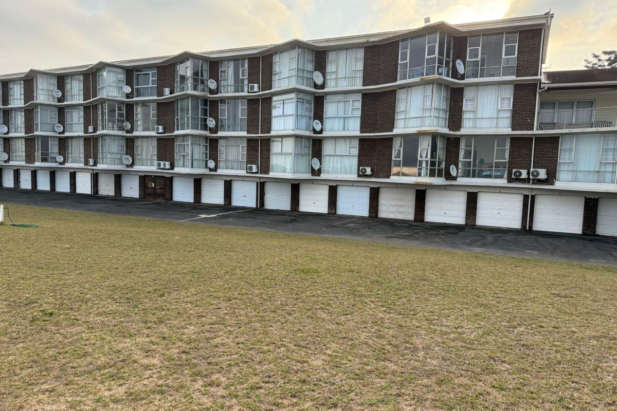 Rear view of a multi-story apartment complex featuring a row of ground-level garages, enclosed balconies, and brick facade construction.