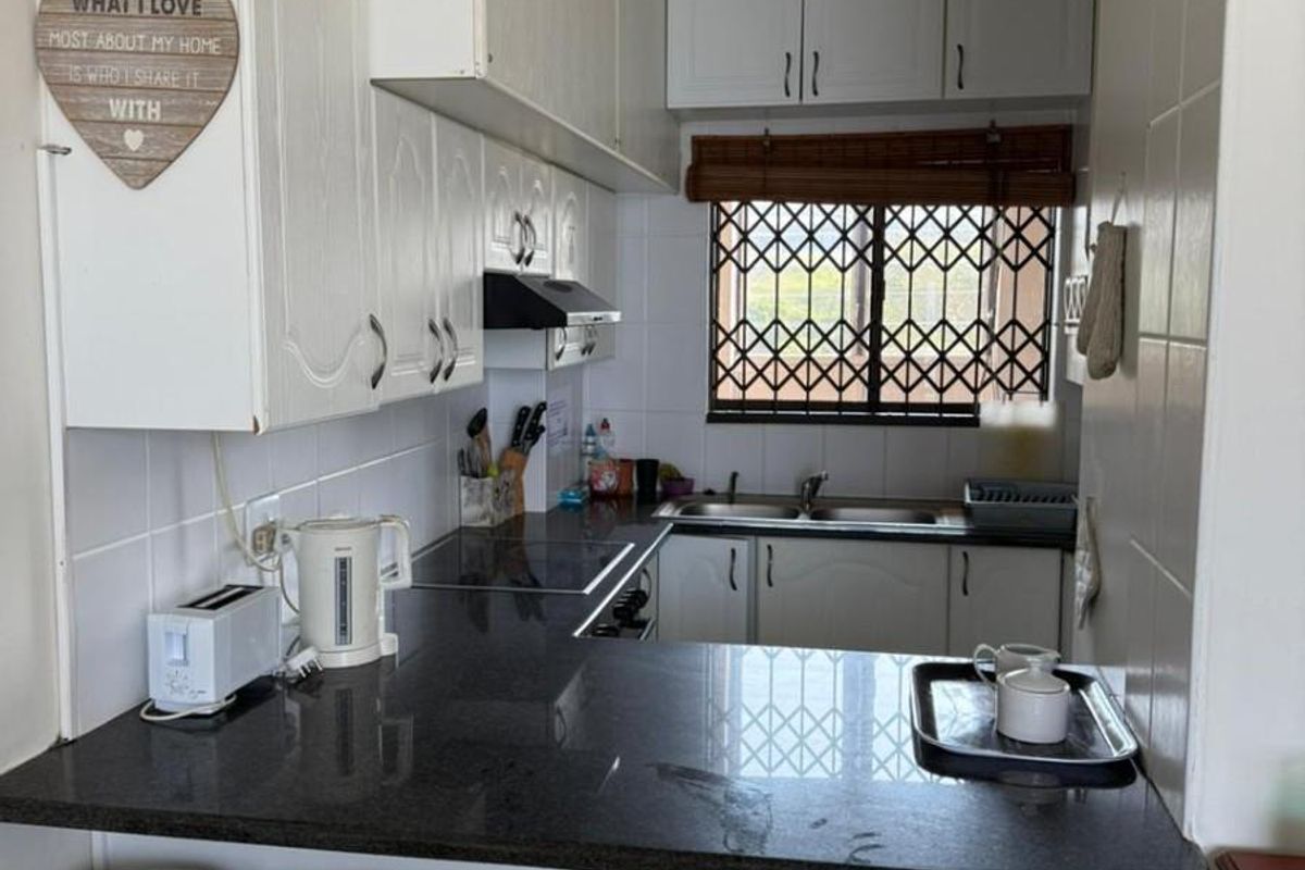 Compact kitchen featuring granite countertops, ample built-in cabinetry, a double sink, and a breakfast bar area with a window security gate.