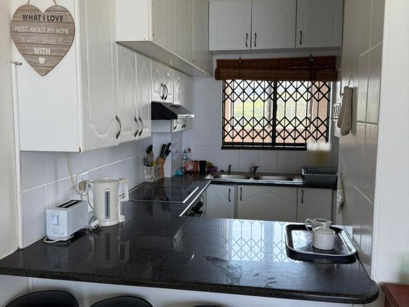 Compact kitchen featuring granite countertops, ample built-in cabinetry, a double sink, and a breakfast bar area with a window security gate.