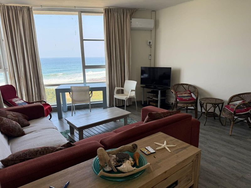 A bright living room featuring large windows with ocean views, laminate flooring, and a wall-mounted air conditioning unit.