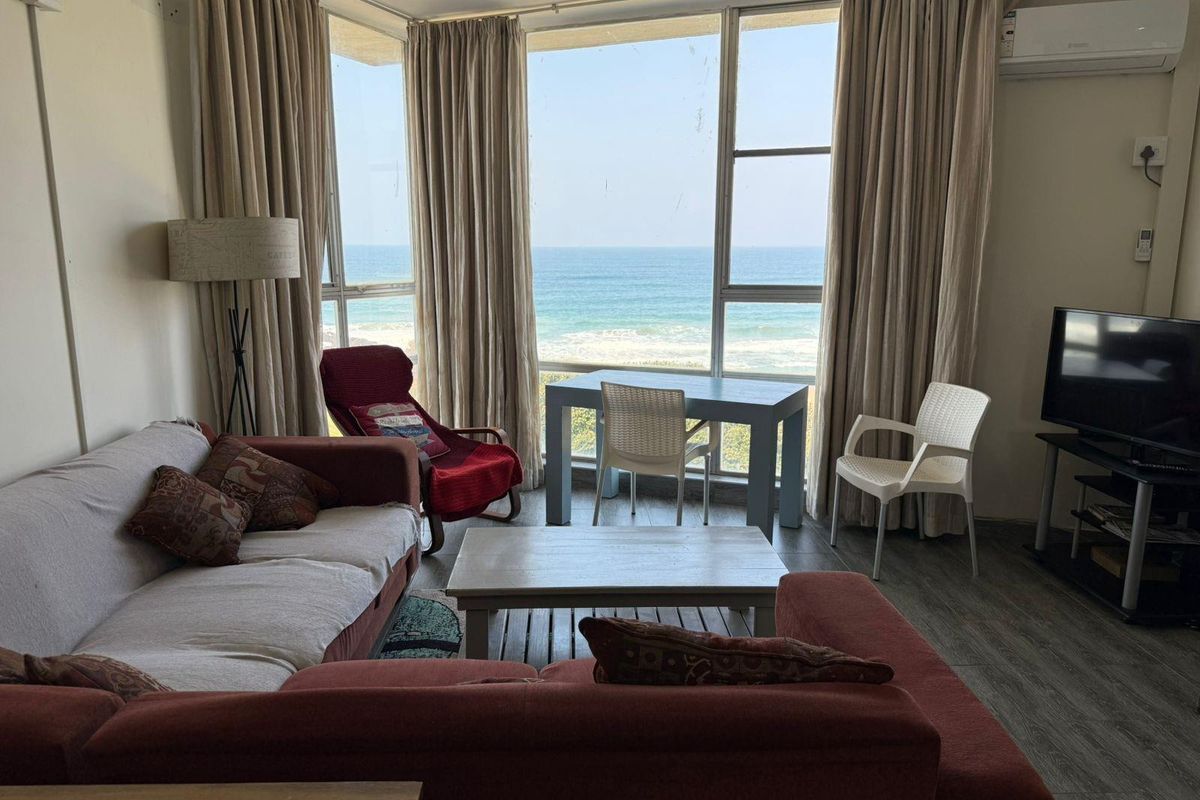 A living room featuring large floor-to-ceiling windows with direct ocean views, laminate flooring, and a wall-mounted air conditioning unit.
