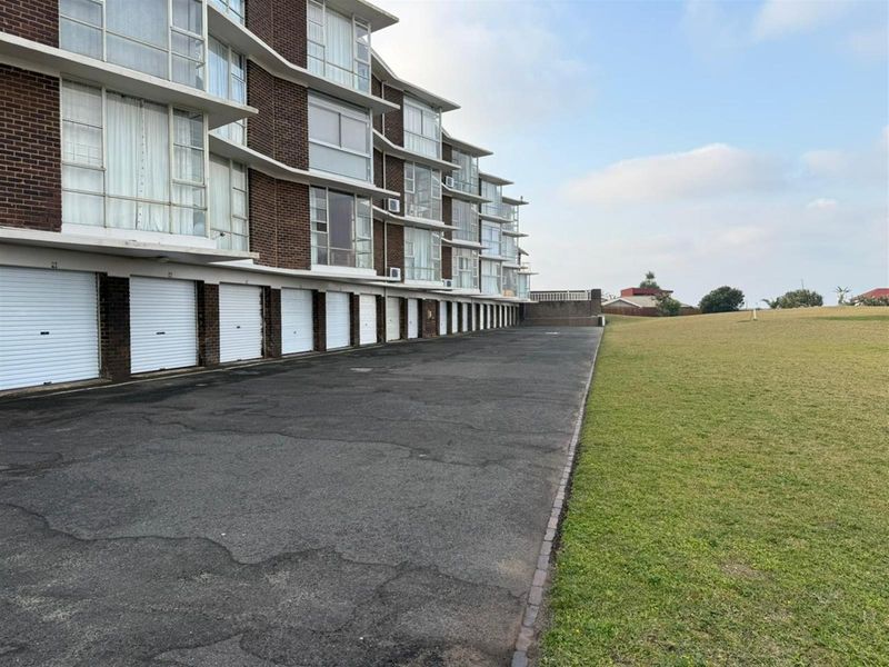 Exterior view of an apartment complex featuring a row of individual garage doors, an asphalt driveway, and adjacent lawn area.
