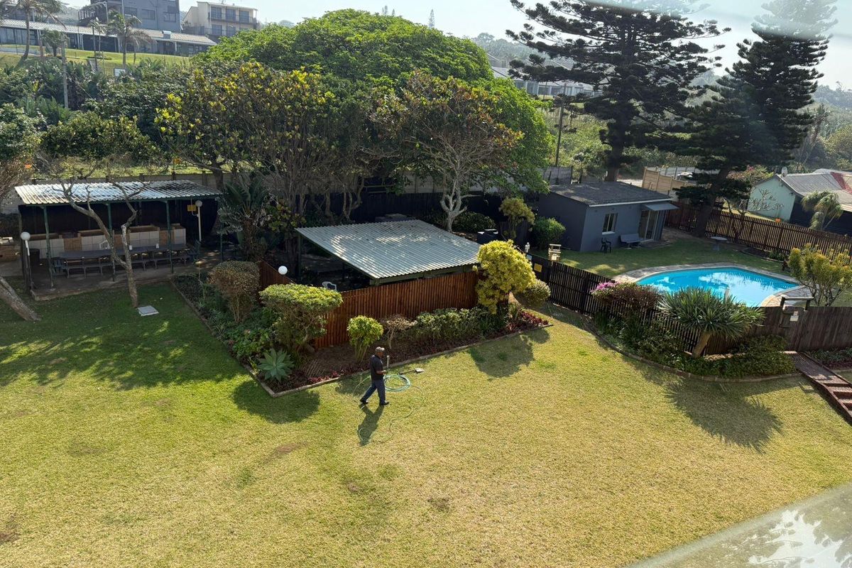 An elevated aerial view of a spacious backyard featuring a swimming pool, a covered patio area, and a well-maintained garden.
