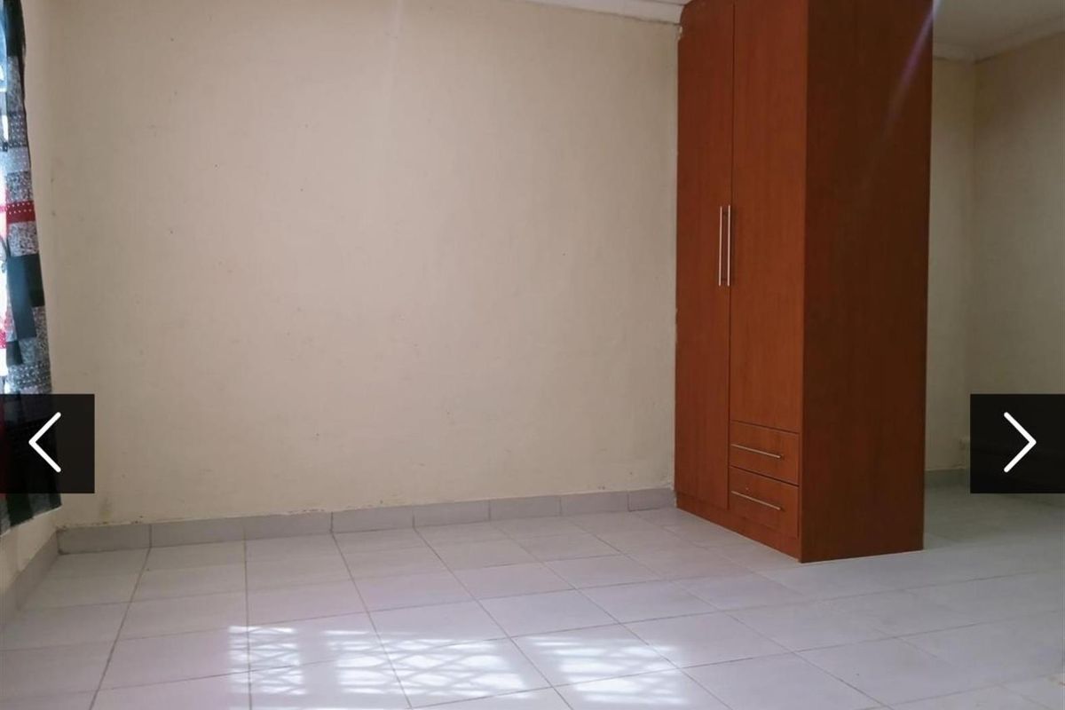A simple, empty bedroom featuring tiled flooring and a built-in wooden wardrobe.