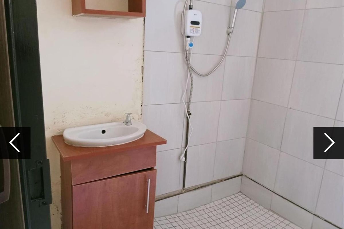 A compact bathroom featuring a vanity basin and a shower enclosure with an electric shower unit, requiring cosmetic repairs to wall finishes.